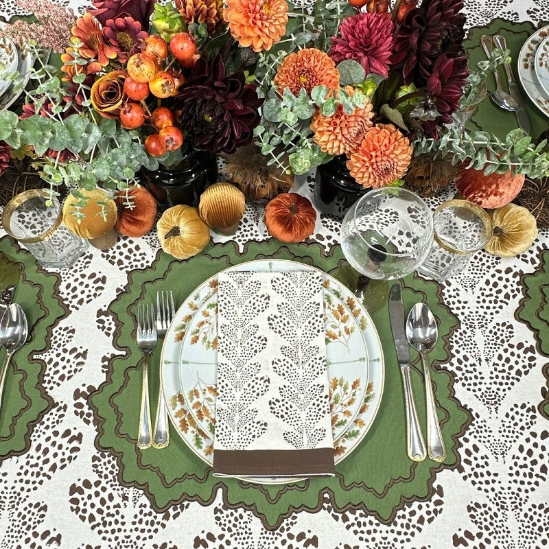 Decorative table setting with autumn-themed centerpiece, plates, and cutlery on a patterned tablecloth. Thanksgiving table, embroidered placemats.