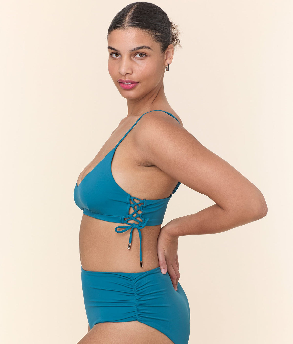 Side view of a model wearing The Elba Bikini Top - Eco Nylon - Ocean by Andie Swim, featuring delicate lace-up side ties with gold cord ends.
