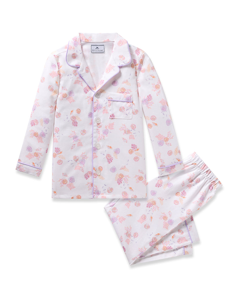 The Petite Plume Kids Twill Pajama in Seashell Splendor features a yarn-dyed cotton floral design with a long-sleeve top and pants. Pastel flowers are accentuated by purple piping on the collar and cuffs, with a front pocket on the top and an elastic waistband on the pants for comfort.