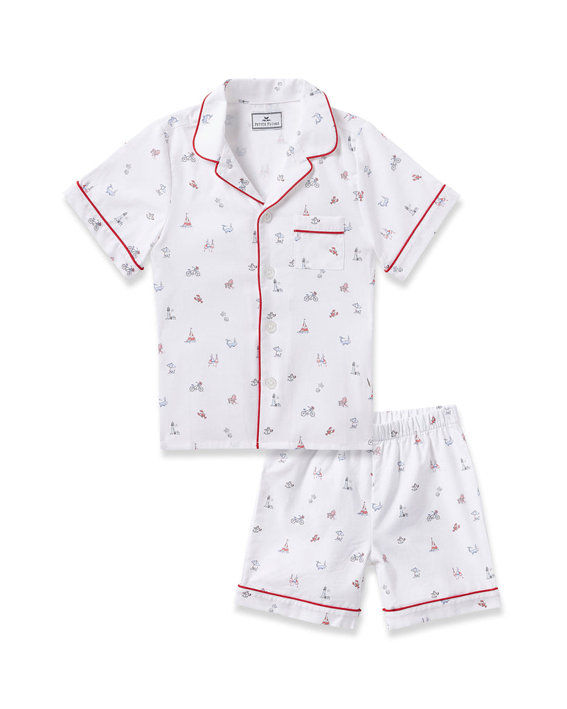 The Kids Twill Short Sleeve Short Set in Coastal Charms by Petite Plume offers white pajamas adorned with sails, anchors, and bicycles. Featuring red piping and a chest pocket, these stylish pieces offer both luxury and flame retardant safety.