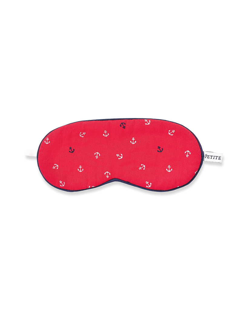 The Kids Twill Sleep Mask in Anchors Away by Petite Plume features red fabric with white anchor patterns, navy trim, a white strap, and a PETITE side tag. Its an ideal accessory for kids wearing red pajamas dreaming of nautical adventures.