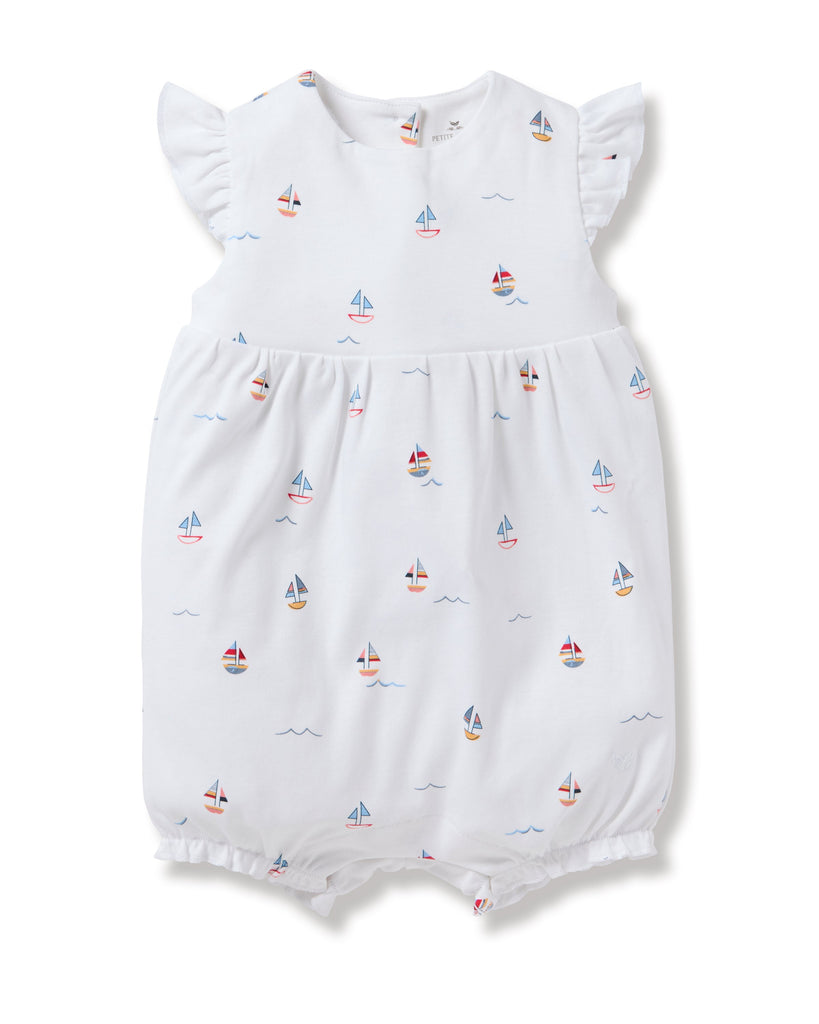 Petite Plumes Babys Pima Isla Play Romper in Bateau is a white romper made from soft Pima cotton, featuring short ruffled sleeves and colorful toy boat patterns. Its slightly puffy design with elastic leg openings offers comfort and style for your little sailor.