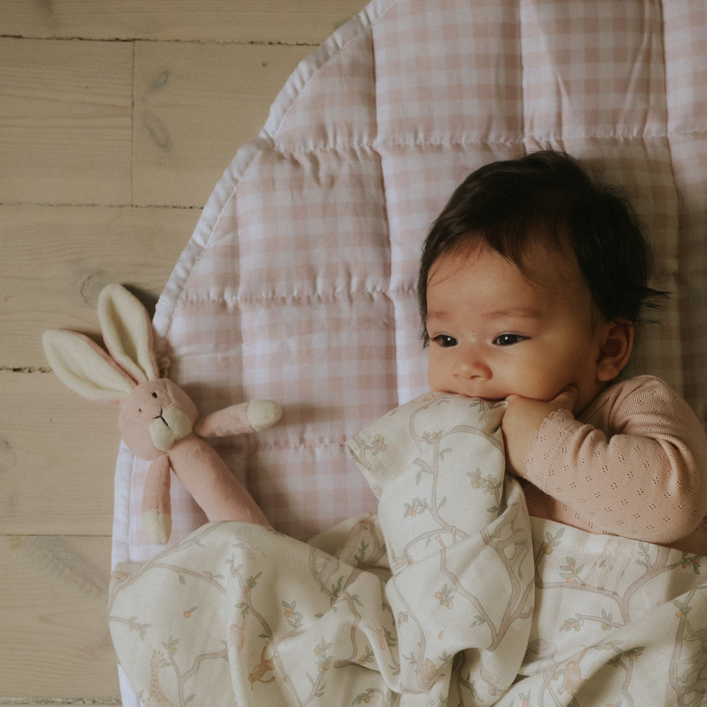 Play Mat in Pink Gingham with baby laying on it with stuffy and swaddle