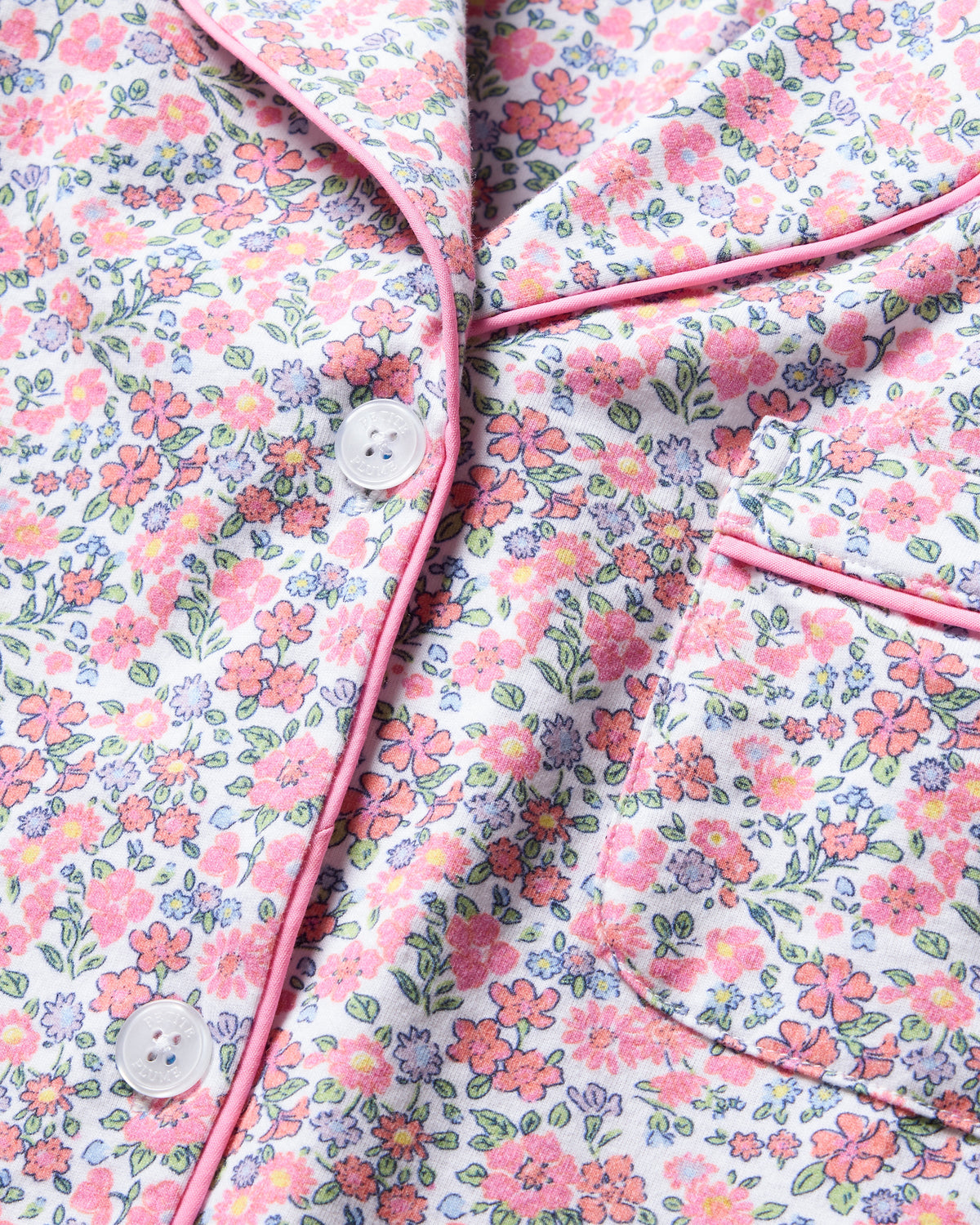 Close-up of Petite Plumes Womens Pima Crop Set in Fleurs de Rose, made of Pima cotton fabric with pink piping, small pink and blue flowers, green leaves, white buttons, and a pocket—perfect for enhancing your bedtime ritual.