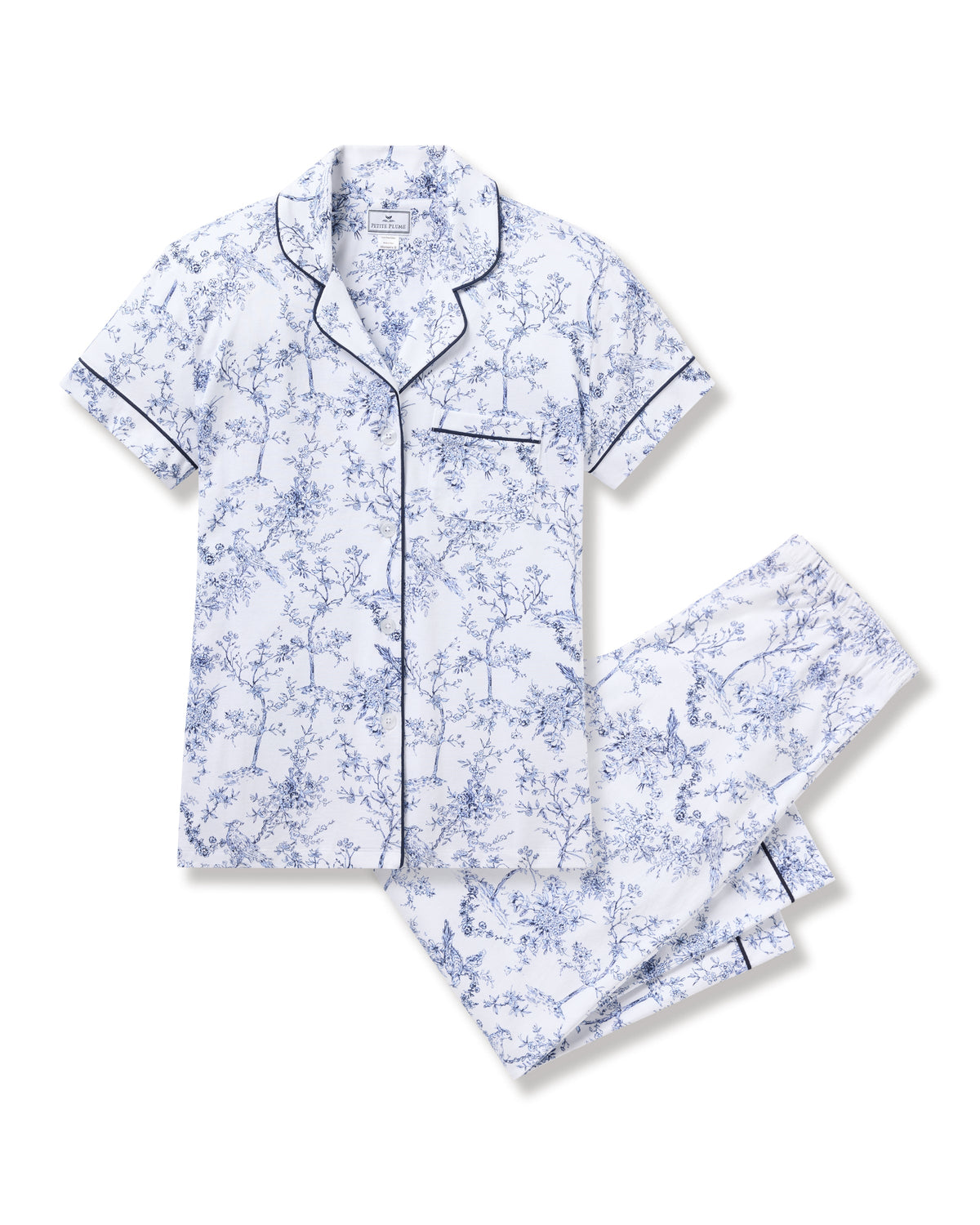 The Womens Pima Crop Set in Timeless Toile by Petite Plume showcases botanical elegance with short sleeves, a white backdrop, and blue floral design. It features a button-up shirt with a chest pocket and matching pants, both outlined with dark piping for classic sophistication.