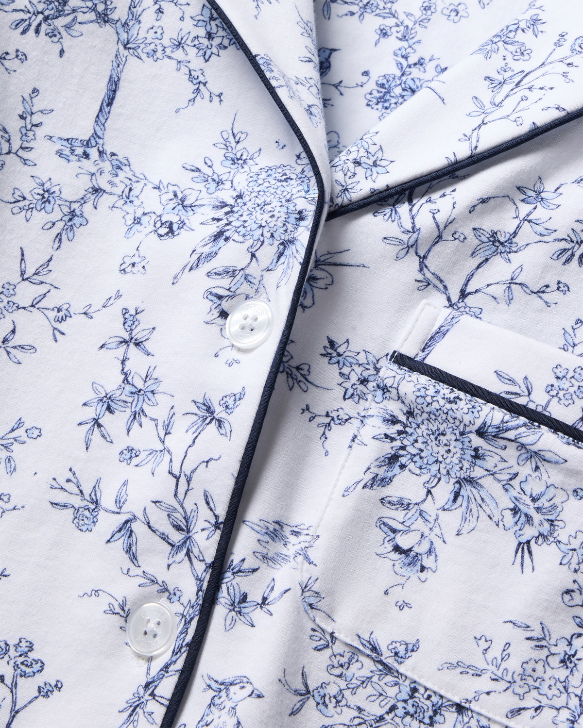 The Womens Pima Crop Set in Timeless Toile by Petite Plume showcases a classic print on white fabric with intricate blue floral motifs. Dark trim, buttons, and a pocket enhance its botanical elegance and sophisticated detail.