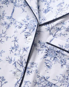 The Womens Pima Crop Set in Timeless Toile by Petite Plume showcases a classic print on white fabric with intricate blue floral motifs. Dark trim, buttons, and a pocket enhance its botanical elegance and sophisticated detail.