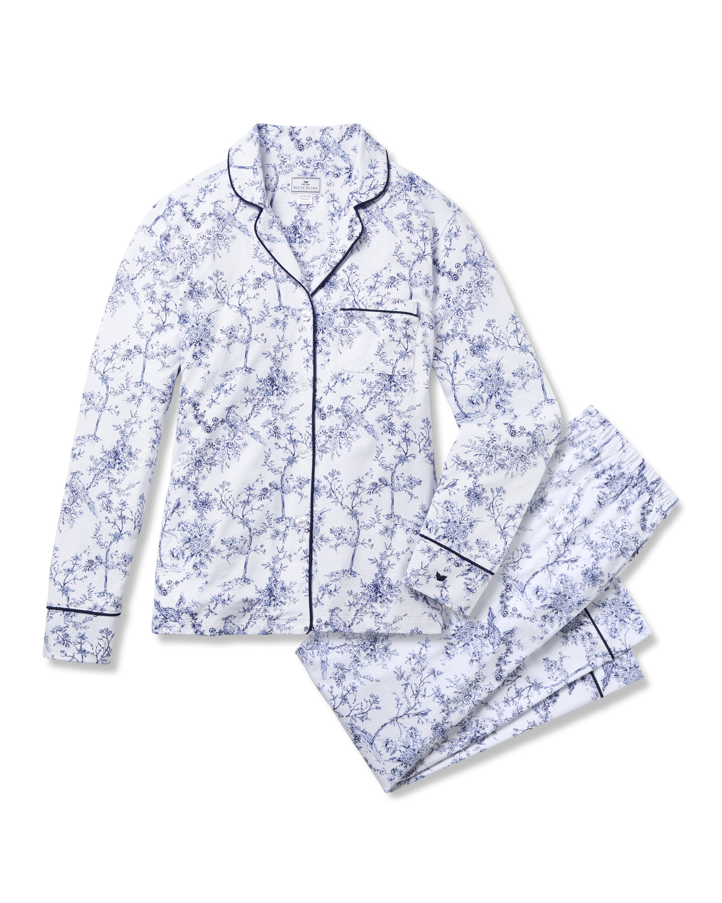 The Womens Pima Pajama Set in Timeless Toile by Petite Plume is a white sleepwear ensemble featuring a blue floral print. It includes a long-sleeved button-up top with chest pocket and matching pants, accented with dark trim for added classic elegance.