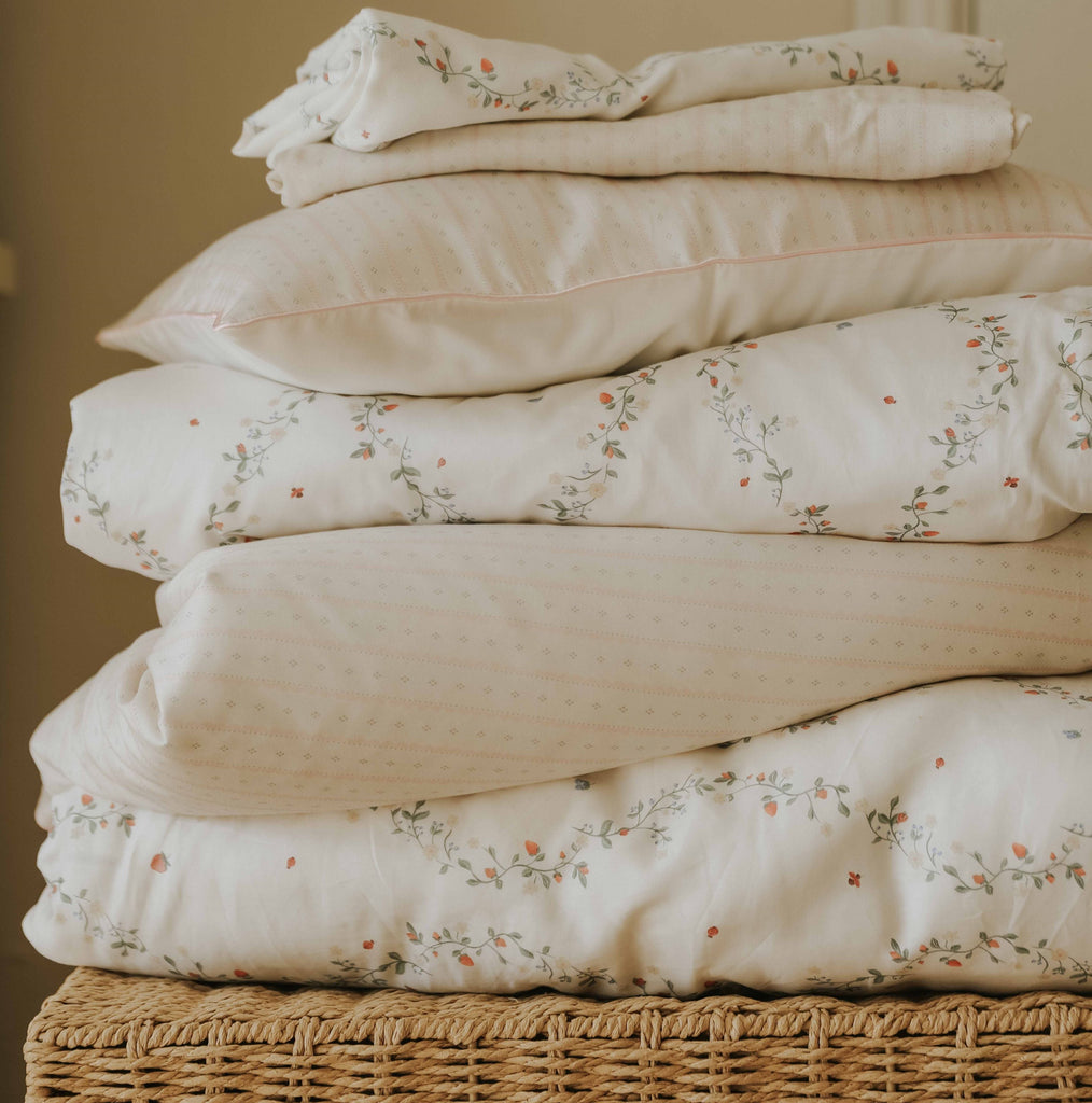 Petal Scallops Toddler Pillow in Pink displayed stacked on top of wicker  basket.