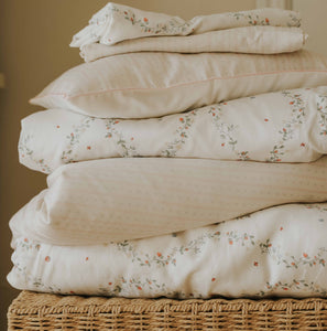 Petal Scallops Toddler Pillow in Pink displayed stacked on top of wicker  basket.