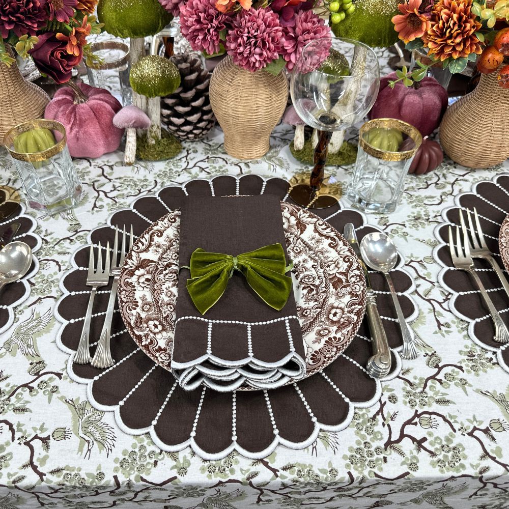 Decorative table setting scalloped linen luxury placemat and matching embroidered napkin in cocoa , bow tie, and floral arrangements.