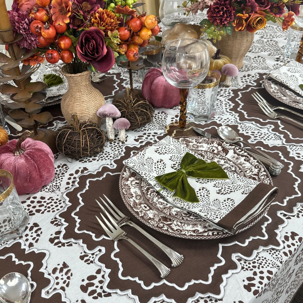 Decorative table setting with pumpkins, flowers, and cutlery on a patterned tablecloth. Luxury embroidered placemat and block print napkin