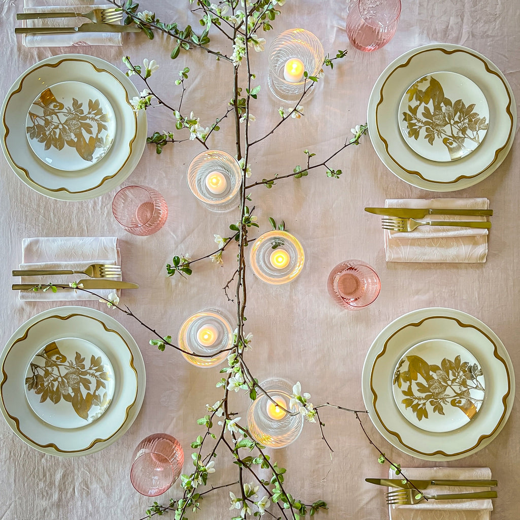 Bird's eye view of a spring tabletop featuring Caskata's Gold Arbor canapé plates on Grace Gold buffet plates around an assortment of Quinn mouth-blown glassware and a flowering branch centerpiece.