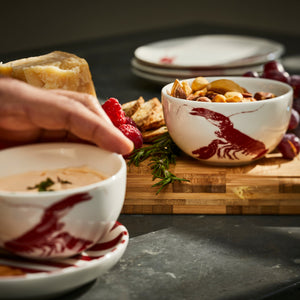A Red Lobster Snack Bowl from Caskata holds nuts on a wooden charcuterie board.