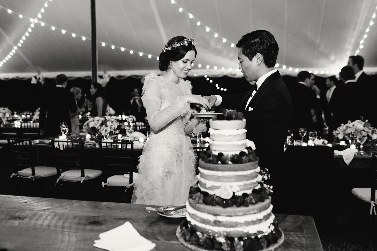 Bride and groom cut a tiered wedding cake at a reception under string lights