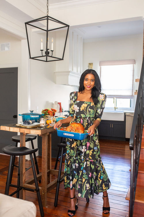 Woman holding a roasted turkey in a blue Le Creuset roaster in a bright kitchen