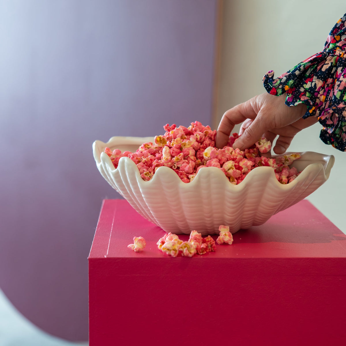 Angled view of Shell Bowl in White Ceramic showcasing its twisted shell shape with popcorn on a red pedestal