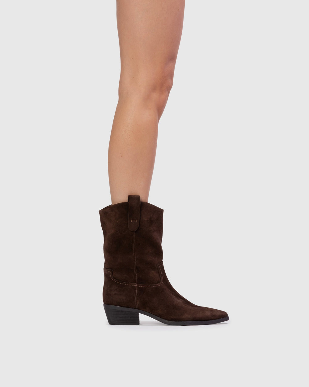 Side view of Casey 55 boot in dark brown suede with western stitching, pull tab and low stacked heel on gray background