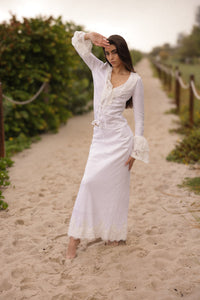 Woman in a white dress standing on a sandy path with greenery around.