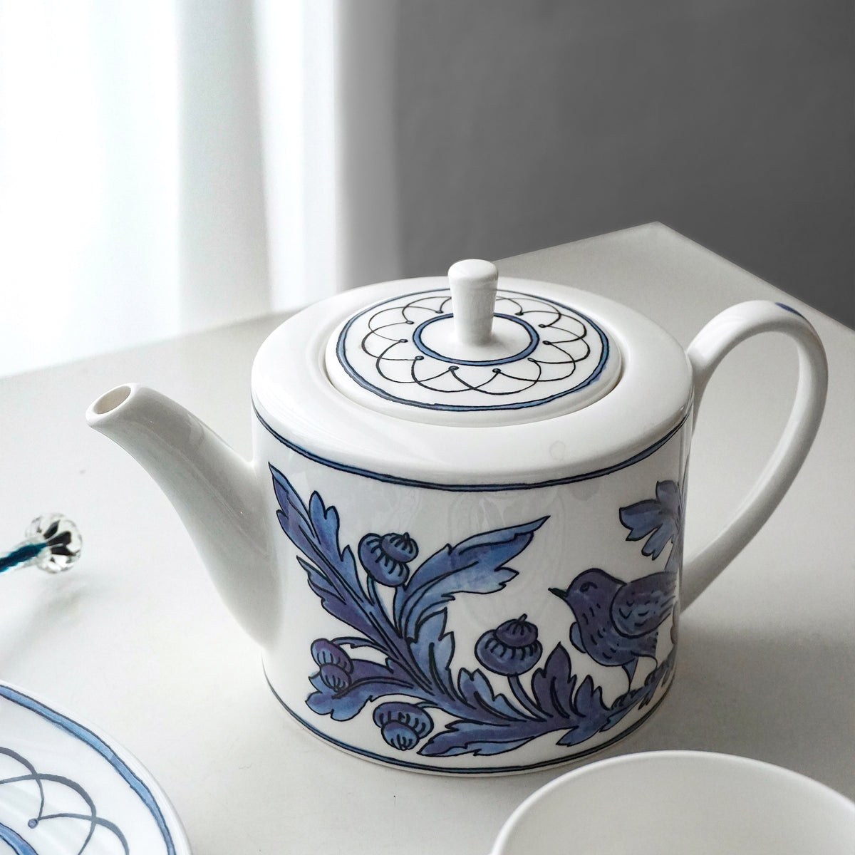 Close-up angled view of Blue Bird Teapot showcasing blue bird and floral decals with a white tabletop background