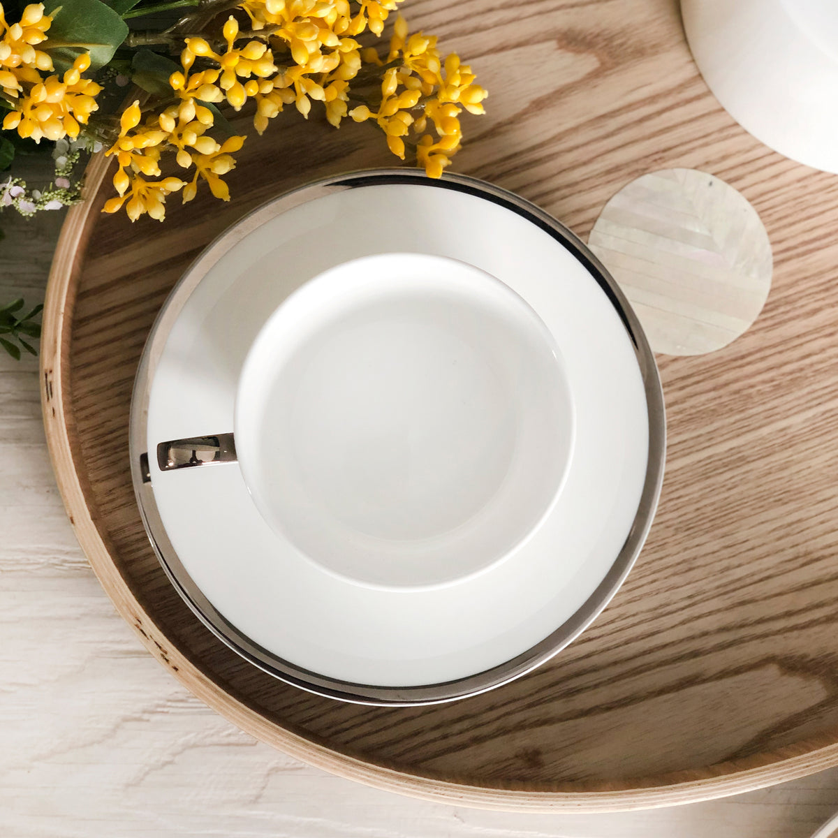 Overhead view of the Platinum Edge Cup and Saucer Set showcasing hand painted platinum rims on a wooden tray with yellow flowers