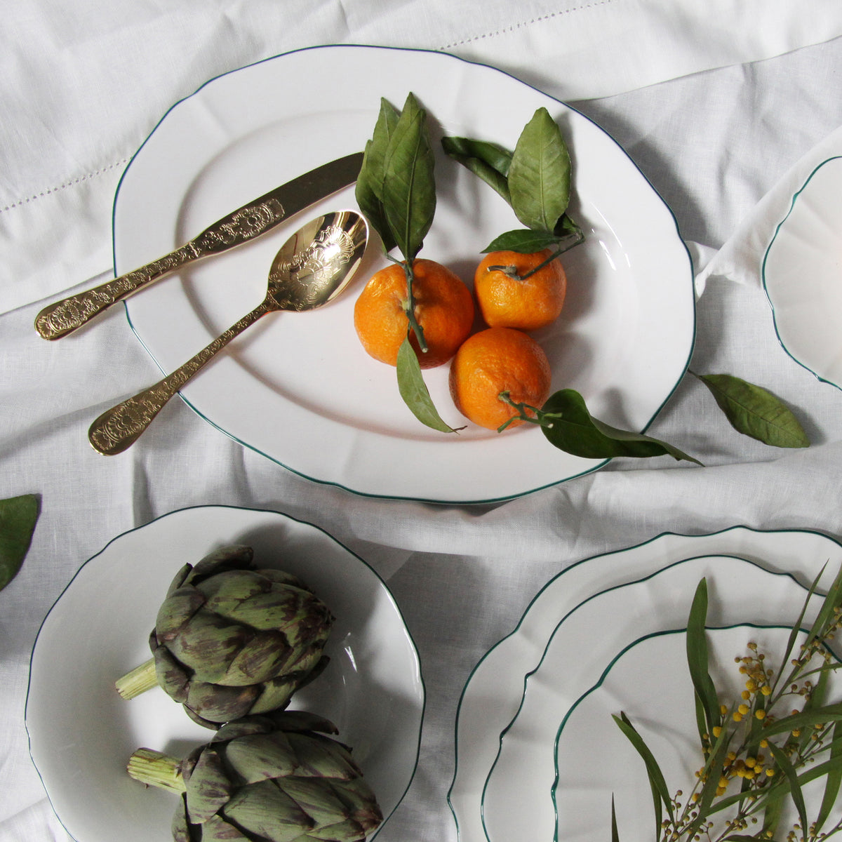 Top view of Amelie Forest Green 14 inch Oval Platter with scalloped edges and hand-painted rim on white tablecloth