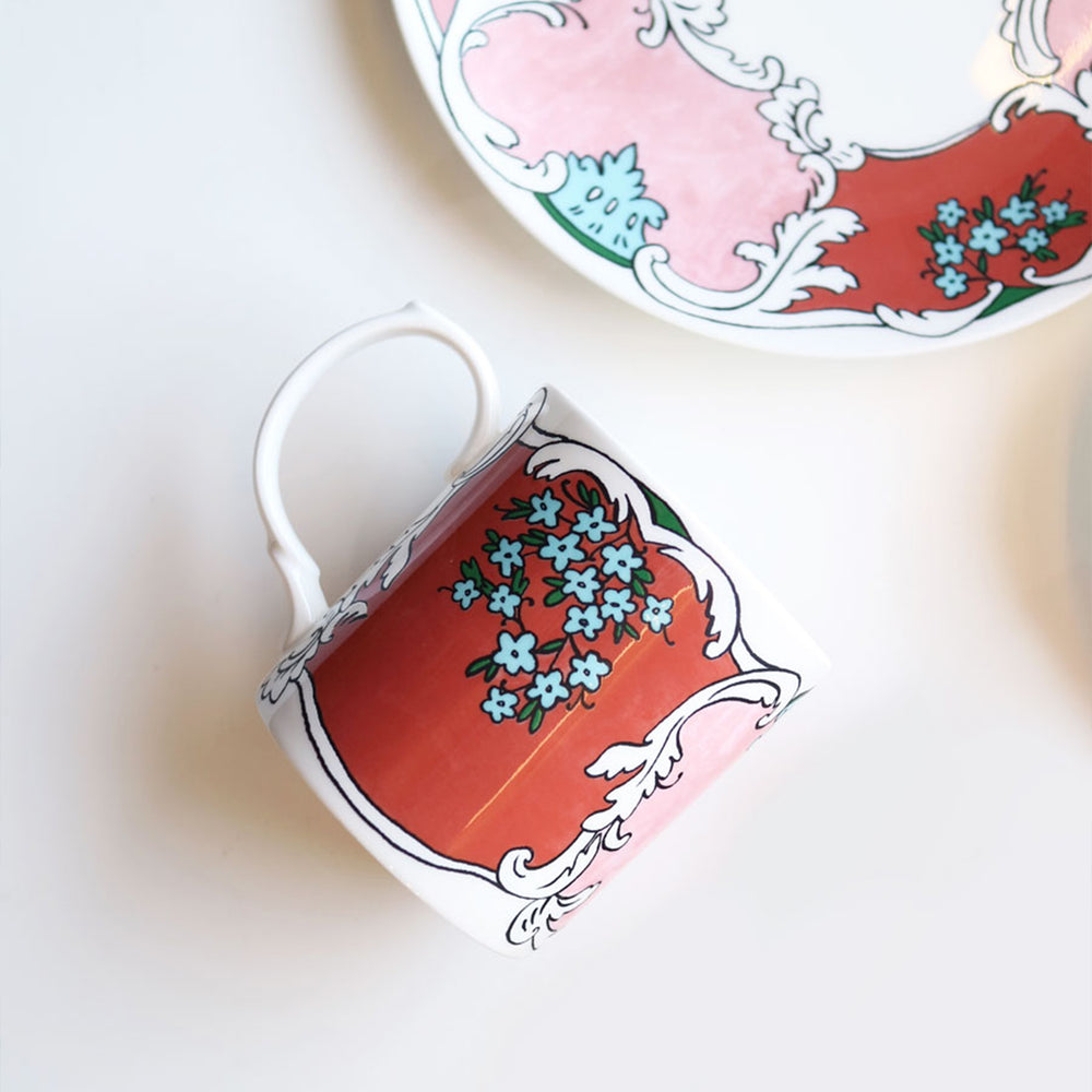 Angled overhead view of Always Camille Mug showing coral-pink panels and blue floral motif on white background