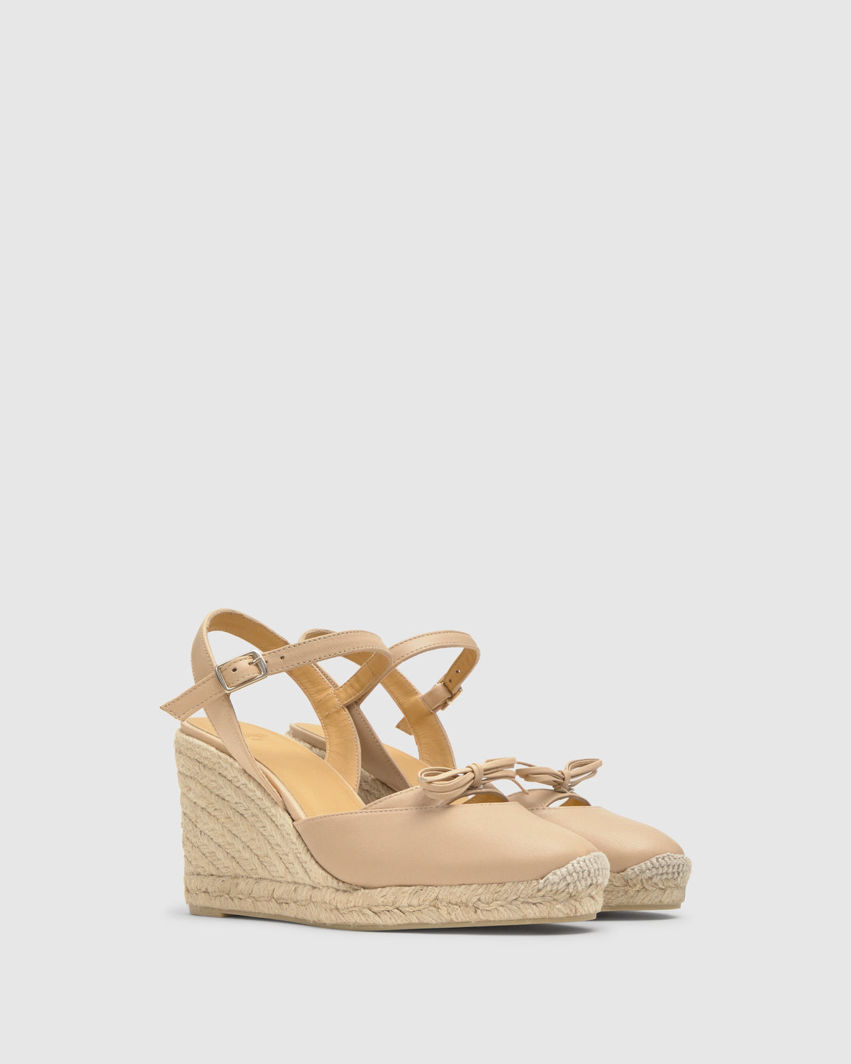 Three-quarter view of Cyra nude leather wedge espadrilles with jute-wrapped wedge, bow detail and ankle strap on light gray