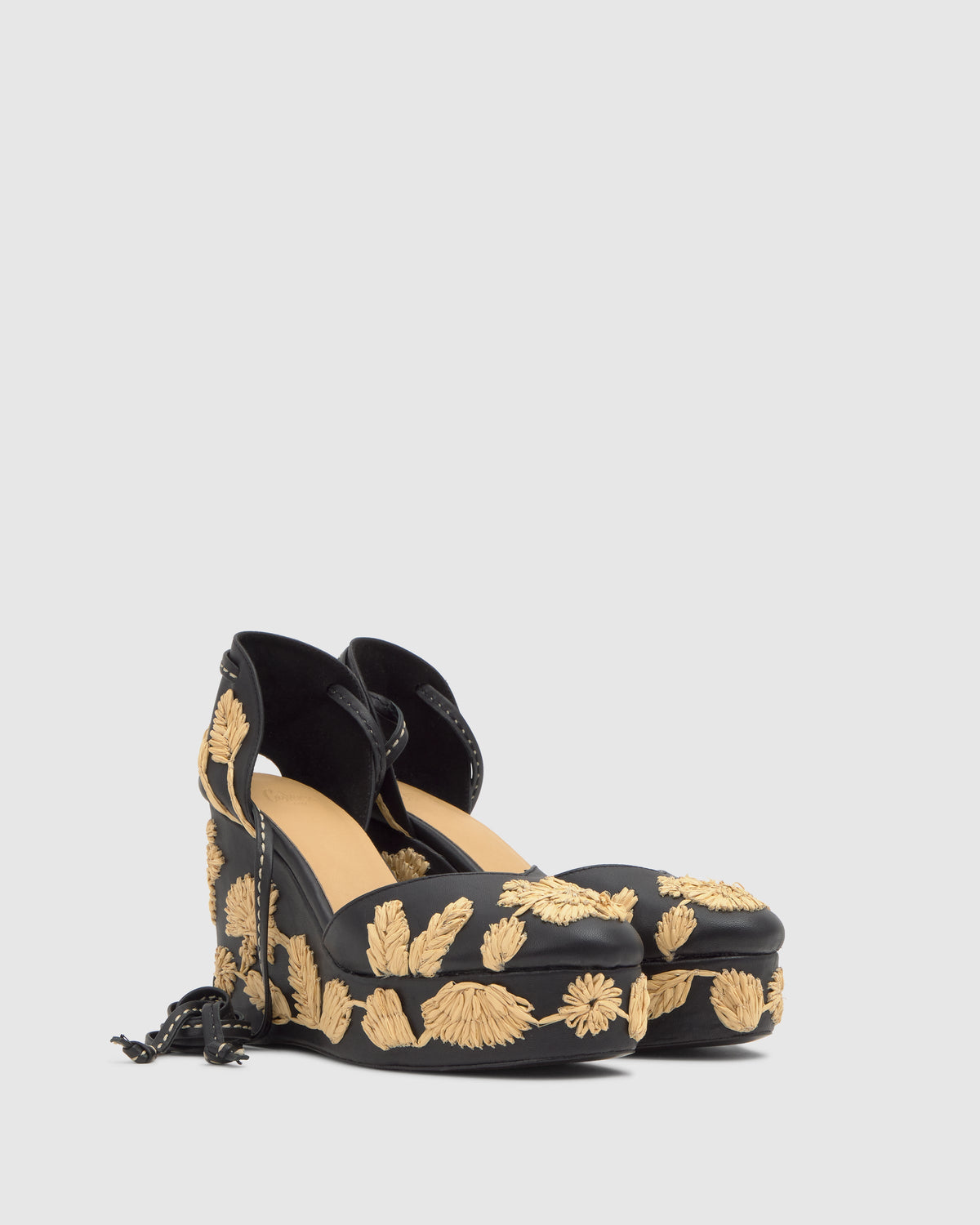 Three-quarter view of Carmela wedges in black with beige floral embroidery, ribbon ankle ties and jute platform
