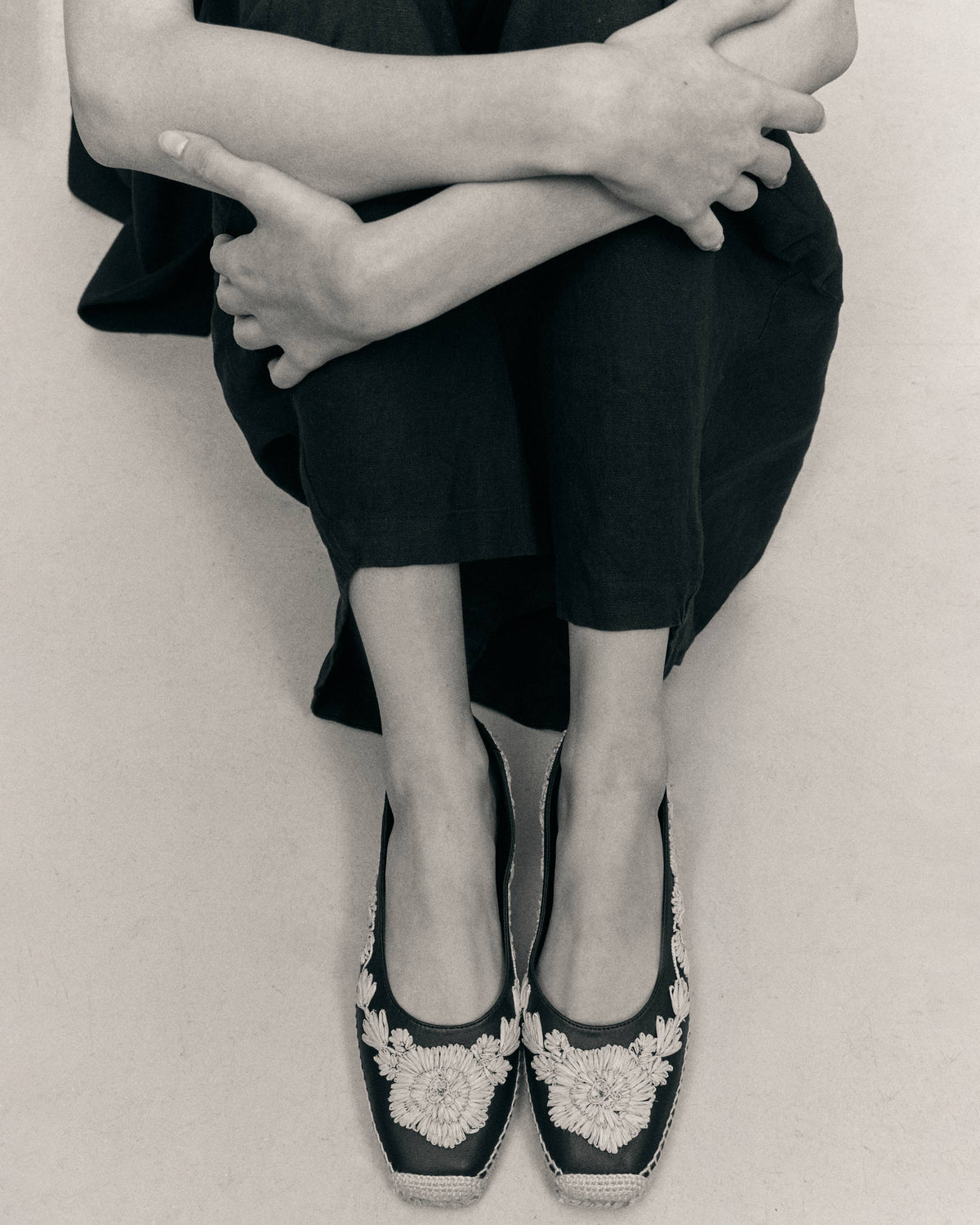 Overhead view of Paris espadrille flats in black showcasing embroidered raffia floral motifs and jute-wrapped sole on a seated model