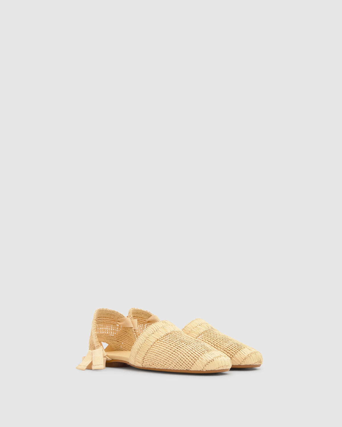 Three-quarter view of Goldie espadrille in natural raffia showcasing woven texture, ribbon tie closure, and braided jute midsole on light gray background