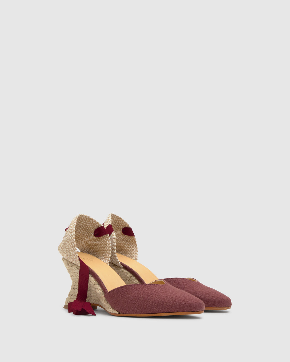 Three-quarter view of Jud espadrille in wine showcasing pointed suede toe, jute wedge heel, and ankle tie ribbons