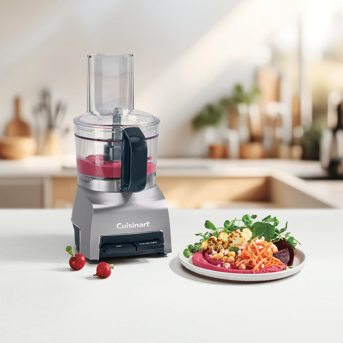 Front view of Cuisinart 5-cup food processor showing clear bowl with a plate of beet hummus on a kitchen counter
