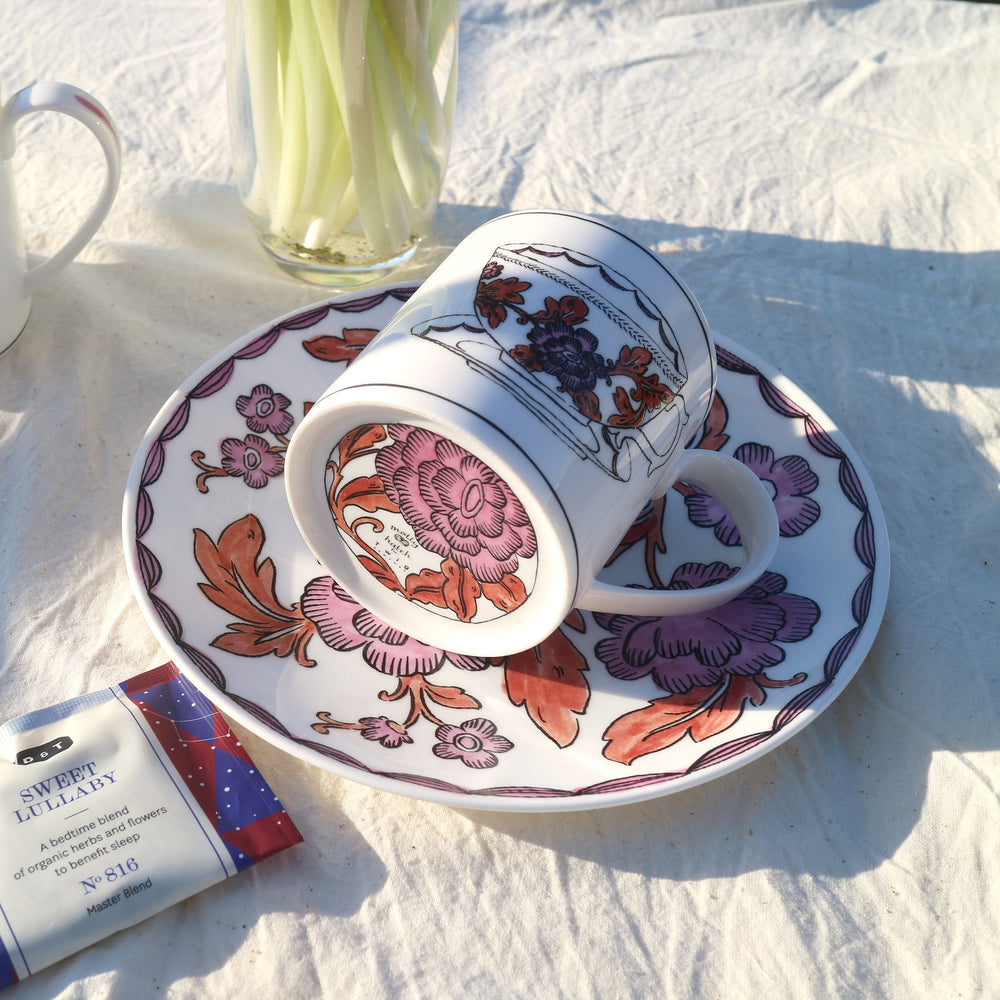 Angled view of Heritage Rosa Rugosa mug and matching saucer showcasing pink and rust floral hand-applied decal on fine bone china with white linen background