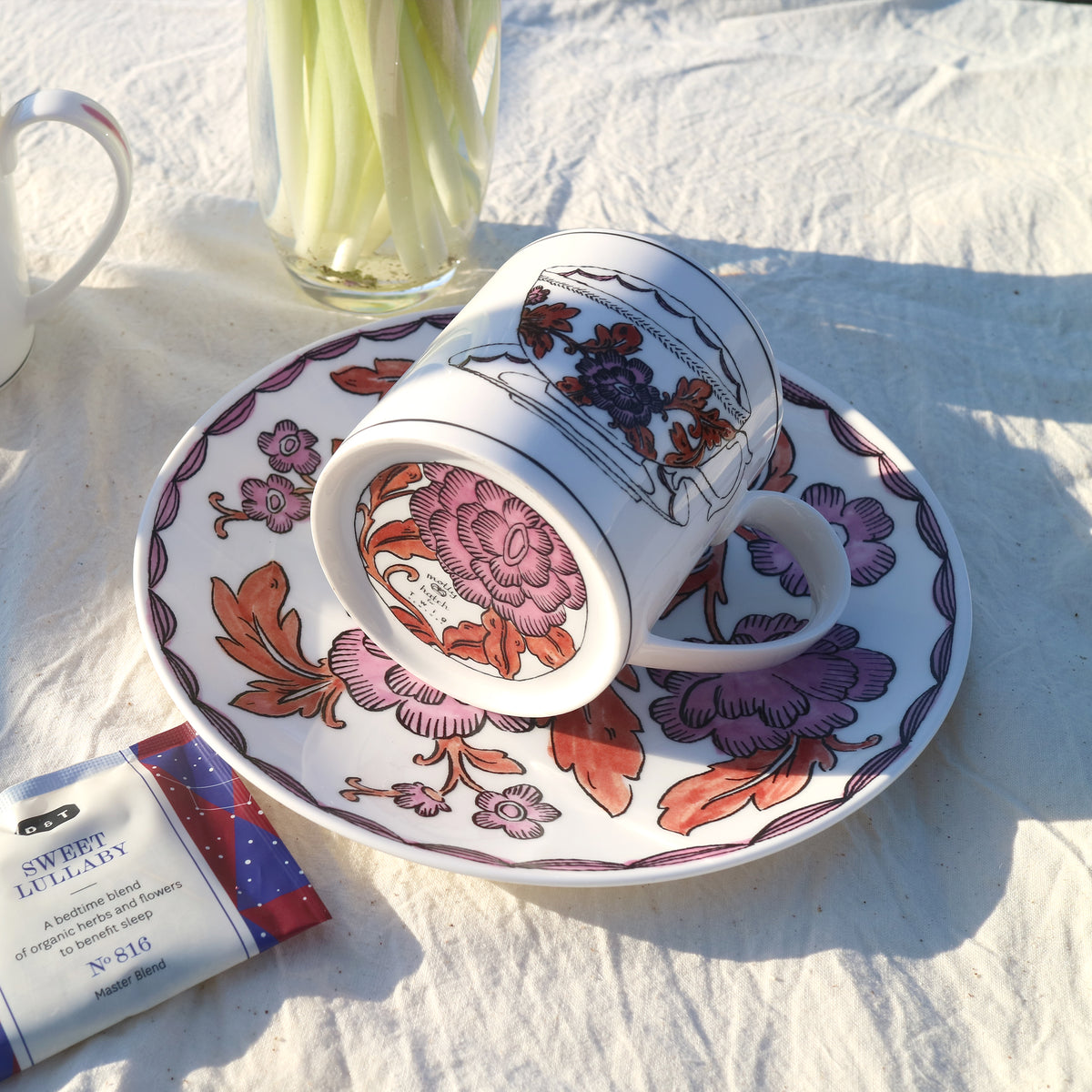 Angled view of Heritage Rosa Rugosa mug and matching saucer showcasing pink and rust floral hand-applied decal on fine bone china with white linen background