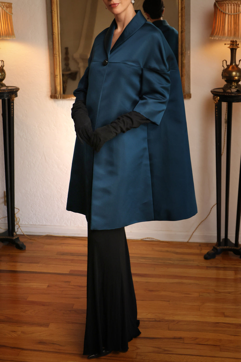 Three-quarter view of Peacock double silk satin cape coat showing cape silhouette and jeweled button closure on a model