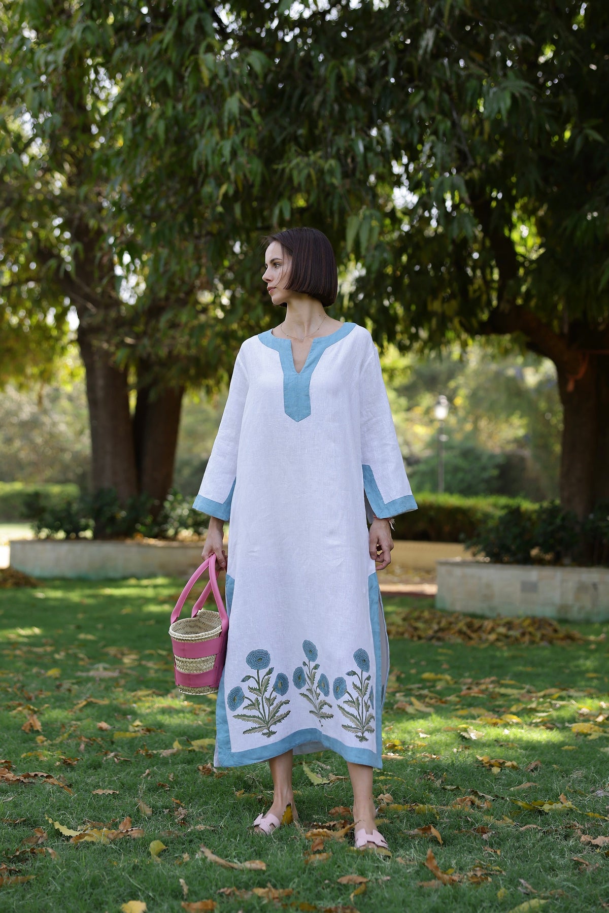 Full-length view of Hampton Caftan in white with blue trim and embroidered flower hem, relaxed fit in a park
