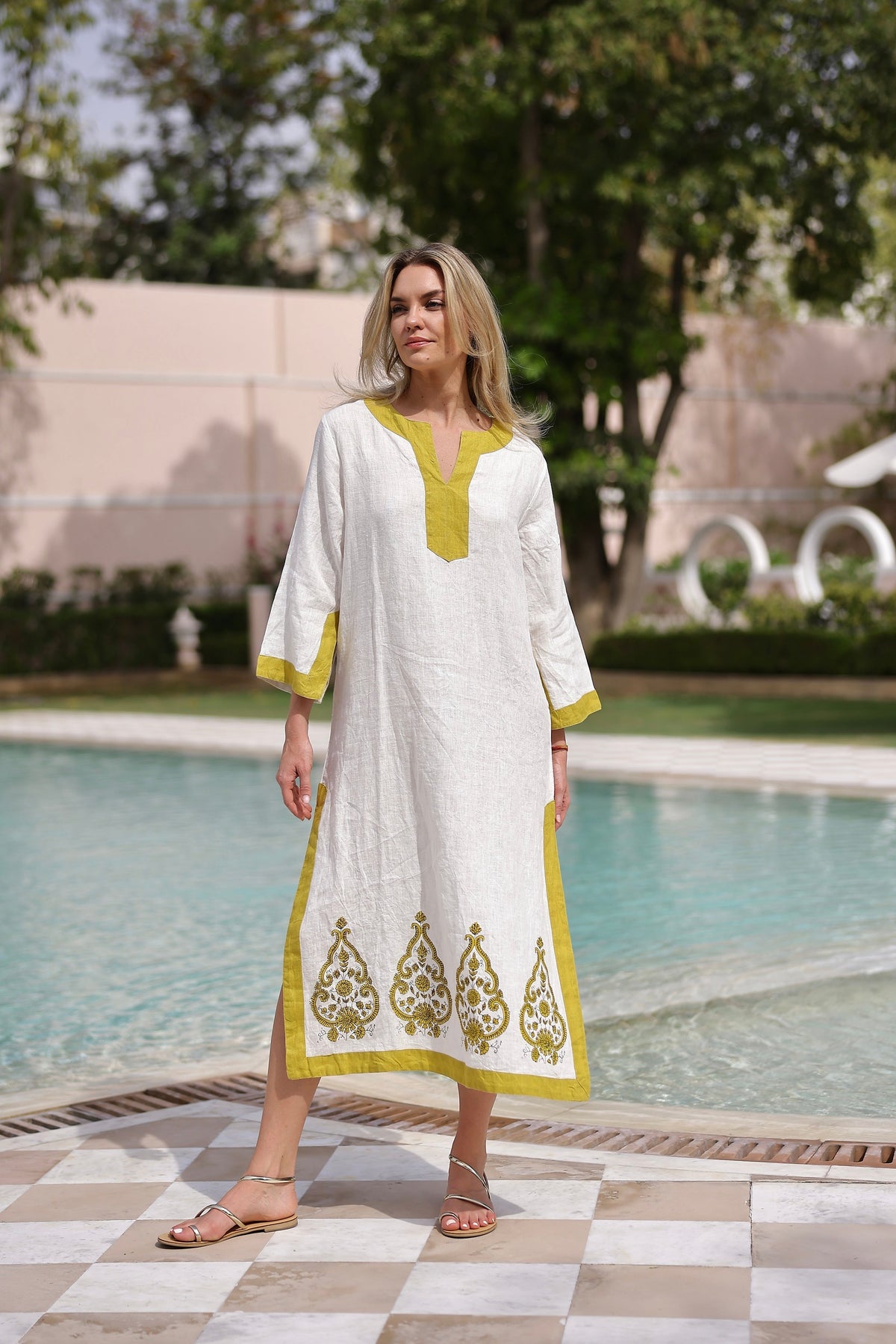 Three-quarter view of Hampton caftan in white with green paisley embroidery, contrast green trim, long sleeves, poolside