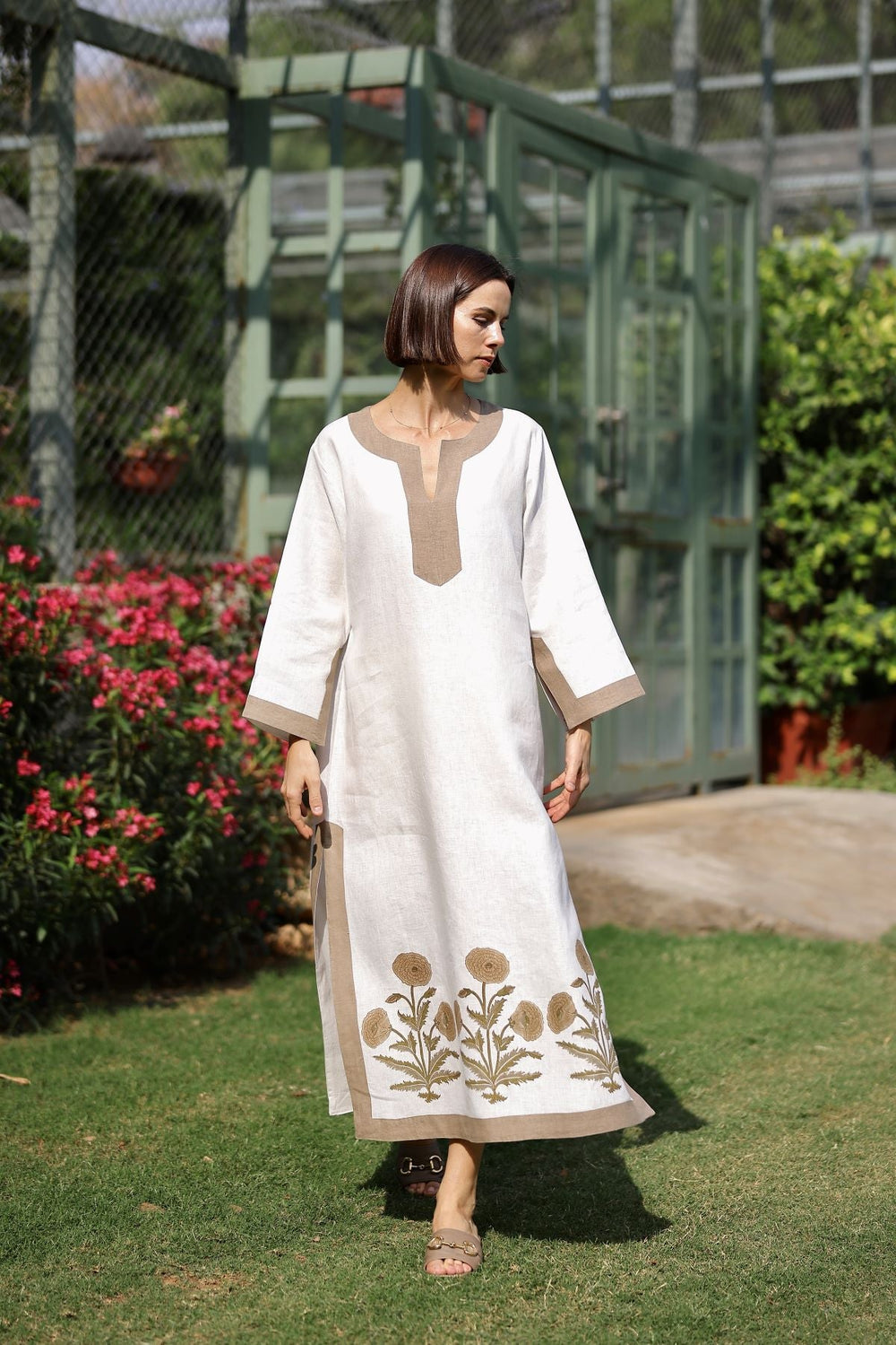 Front view of Hampton Caftan with khaki trim showcasing split neckline and floral embroidered hem in a garden setting