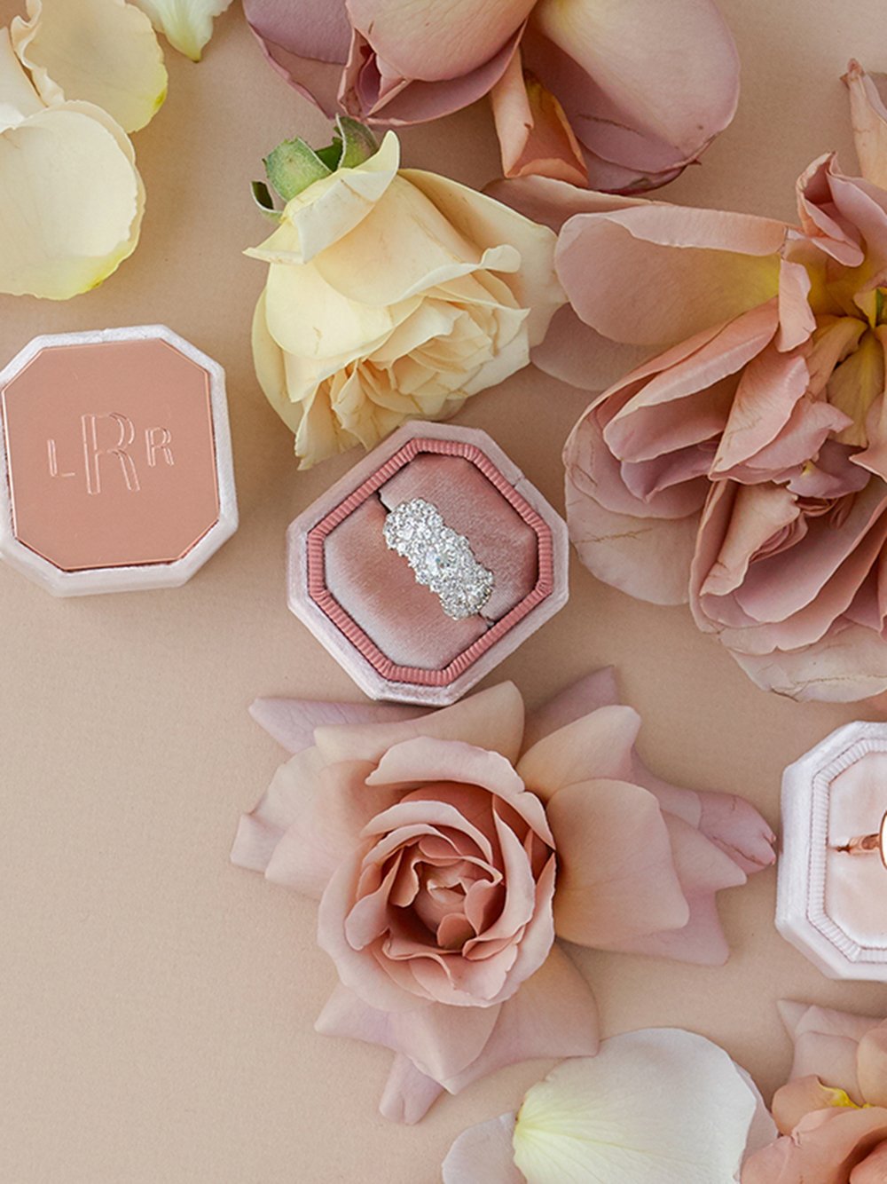 Top view of The Hope Bevel single ring box showing a diamond band in a blush-pink octagon box surrounded by pale pink roses