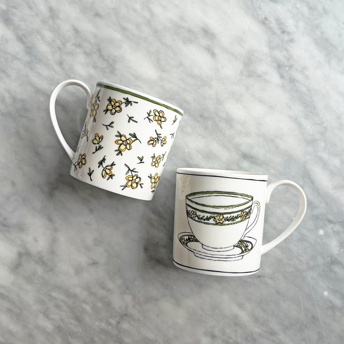 Angled view of Heritage Daisy Chain Mug 2 with hand-applied daisy decals and green rim beside a coordinating mug