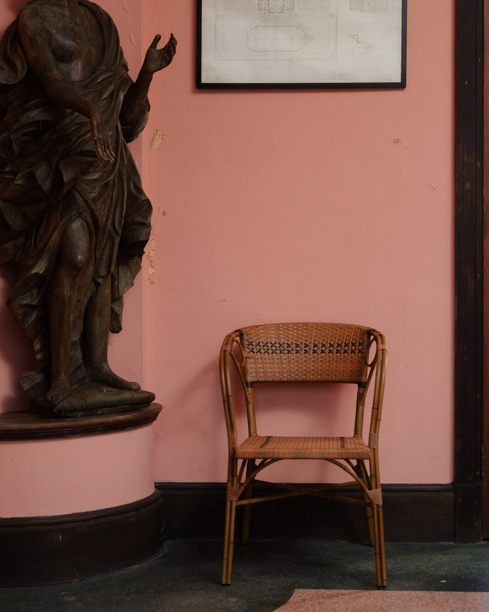 Front view of Juliette armchair showcasing handwoven rattan weave and curved arms against a pink wall and statue background
