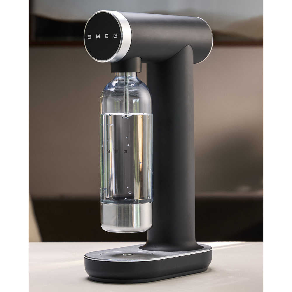Front view of matte black SMEG sparkling water maker with clear Tritan bottle on a kitchen countertop