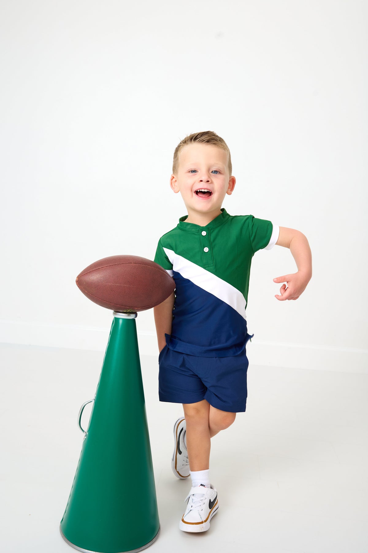 Front view of Cross-Court Blade Shirt on child model showing green and navy color block and blade collar on white background