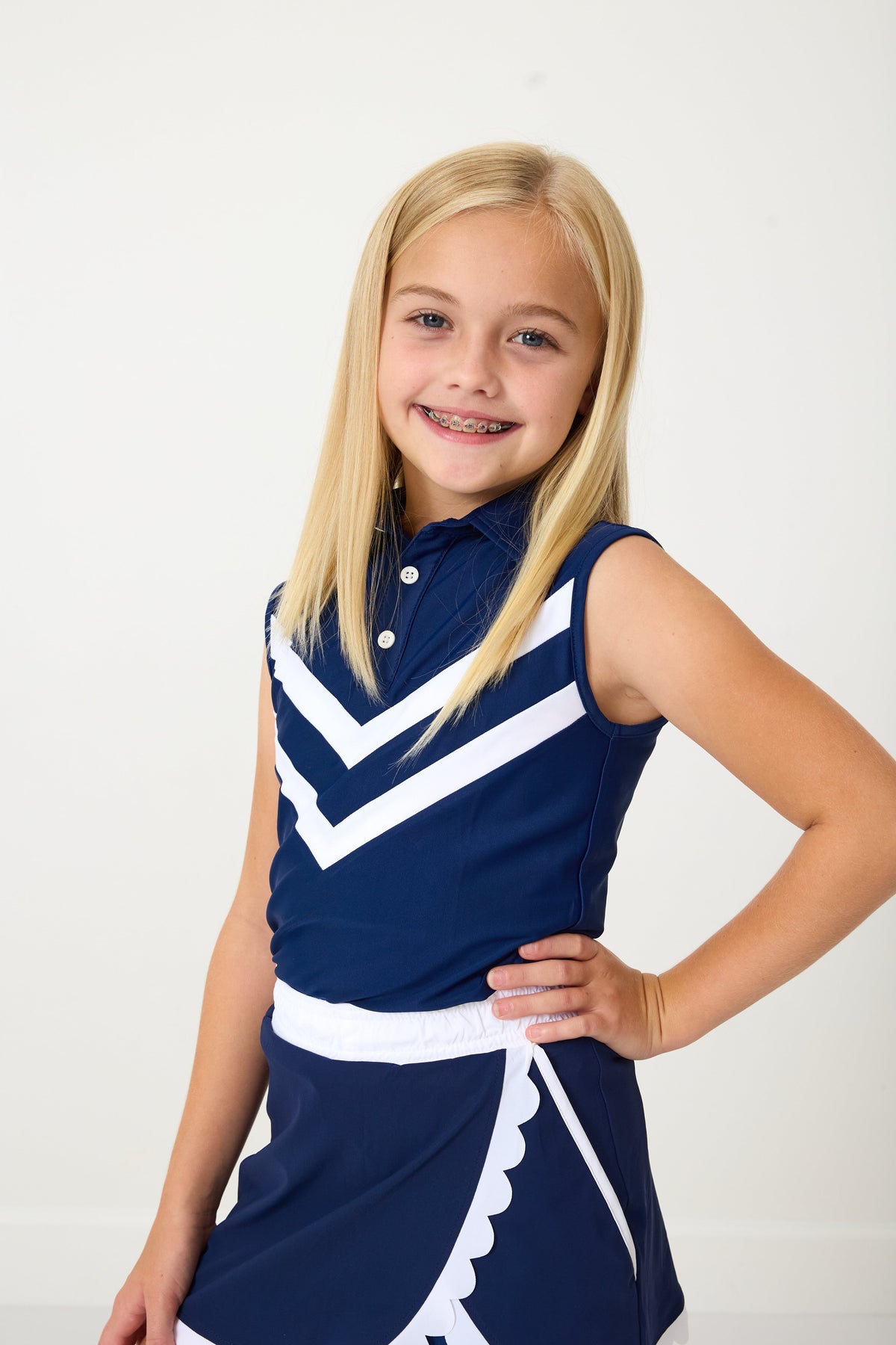 Three-quarter front view of kids navy cheer top showing white V-stripe chevrons and collared sleeveless polo on white background