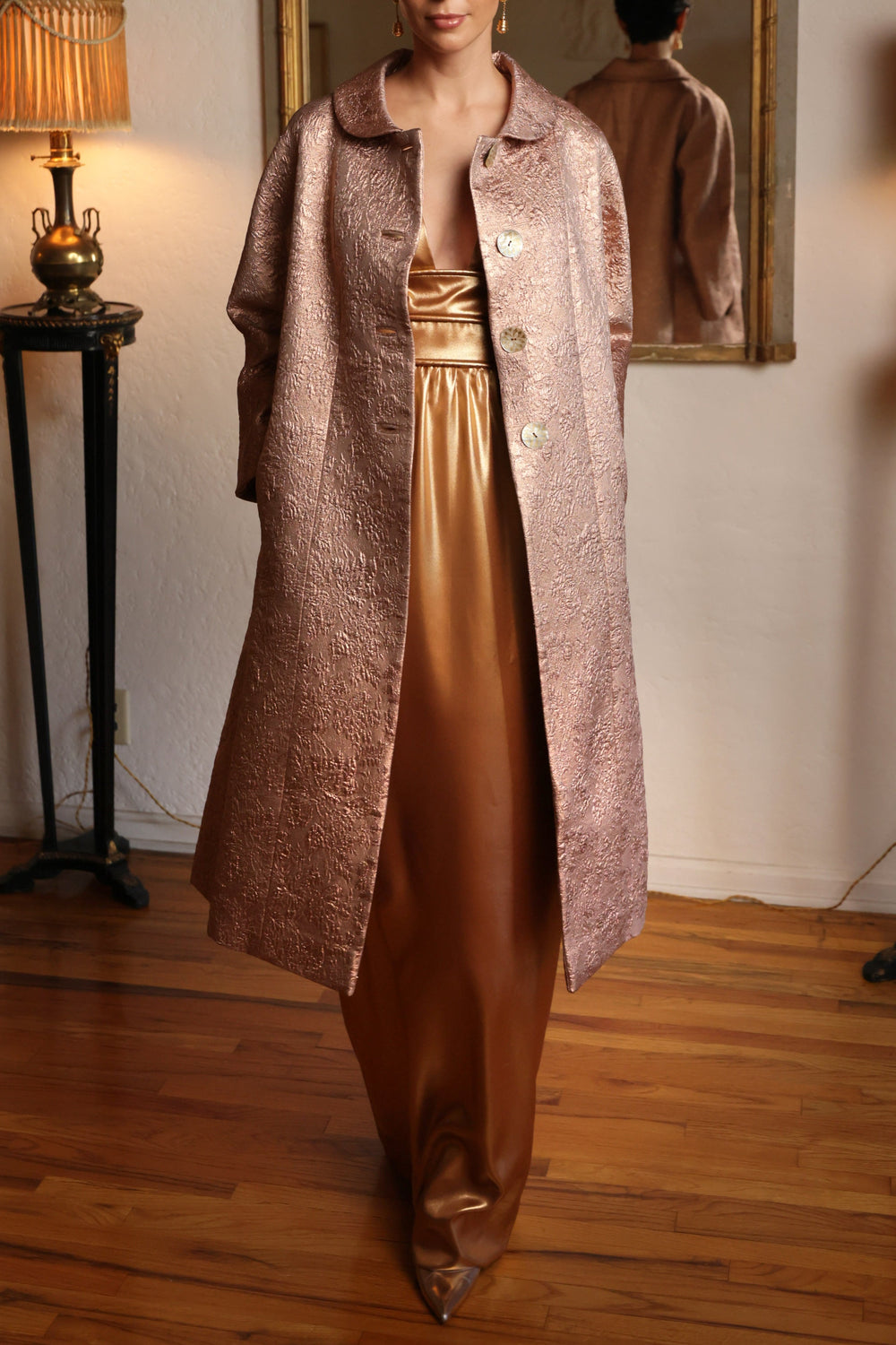 Front view of blush overcoat showcasing textured shimmery brocade, large buttons, and mid-length tailored silhouette worn indoors