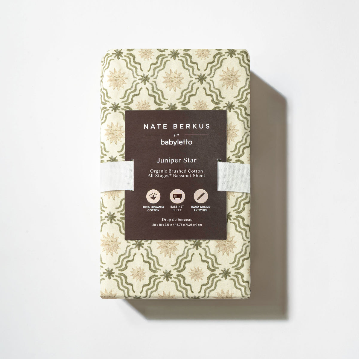 Top view of All Stages Bassinet Sheet in Juniper Star showcasing folded patterned fabric and product label on white background
