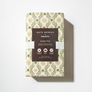 Top view of All Stages Bassinet Sheet in Juniper Star showcasing folded patterned fabric and product label on white background