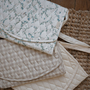 Portable Changing Pad in Beige Gingham, Secret Garden and Ivory laying flat on top of a Jute rug