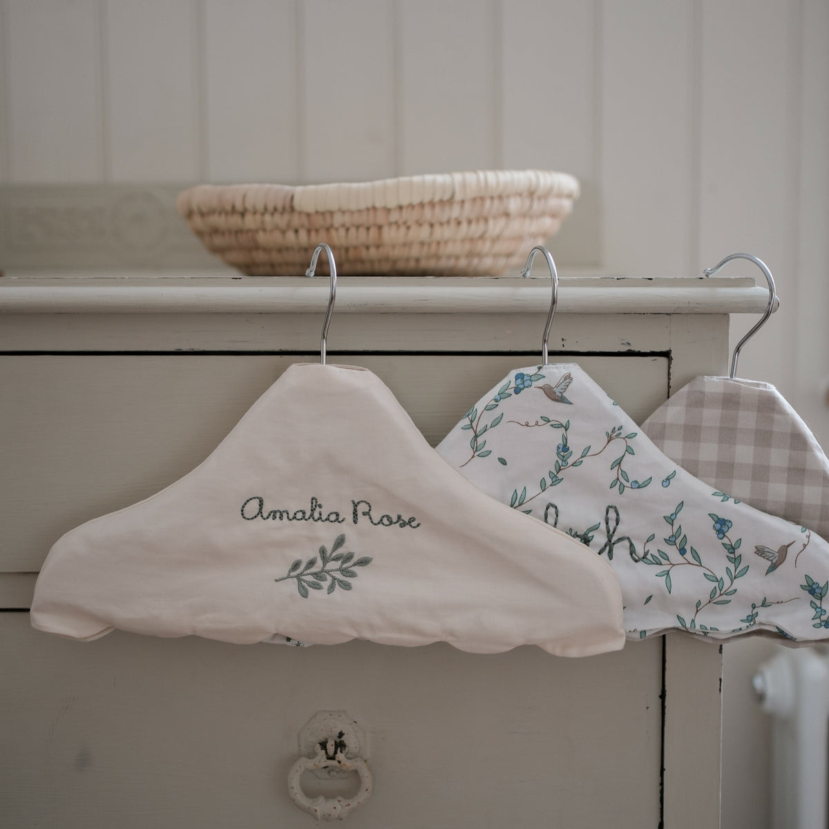 Children's Hanger in Ivory, Secret Garden, and Beige Gingham hanging off top of dresser